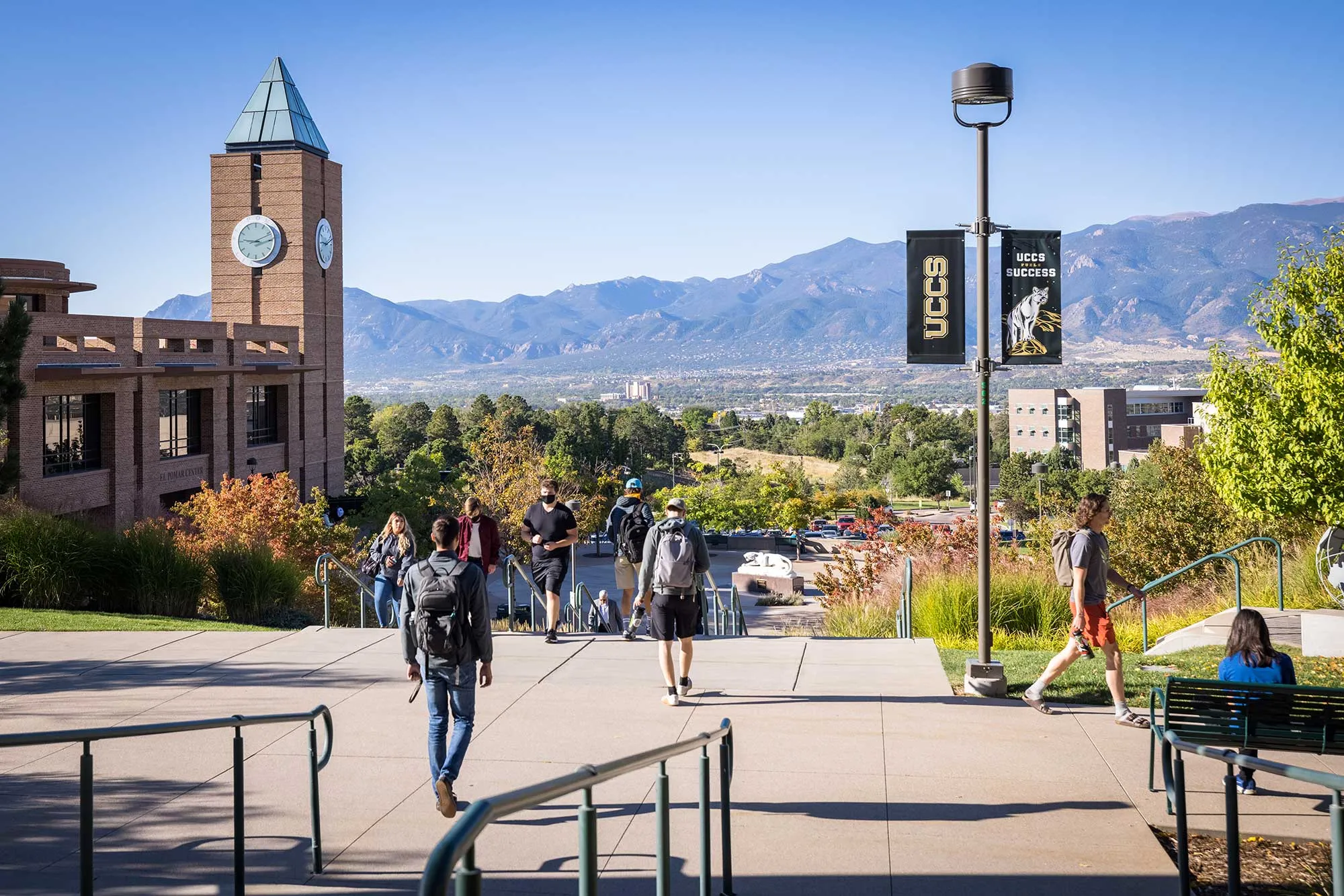 Students walking in front of UCCS plaza facing the mountains with a blue sky.